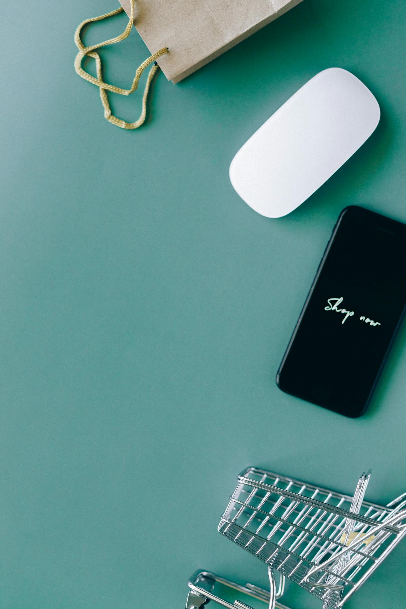 Flat lay of a smartphone, shopping cart, and paper bag representing online shopping and e-commerce.