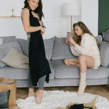 Two women relaxing while trying on new clothing purchases in a cozy living room setting.